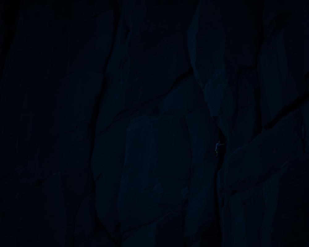 Climber silhouetted on a dark granite wall at dusk